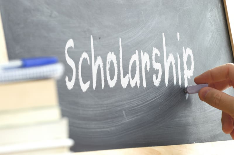 A person writing the word Scholarship on a blackboard. Some scho