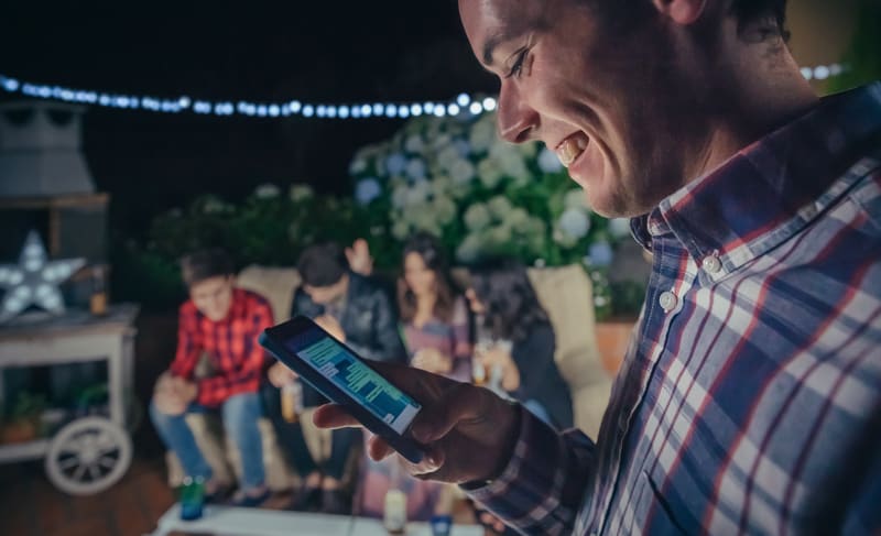 Happy man looking smartphone in a party with friends