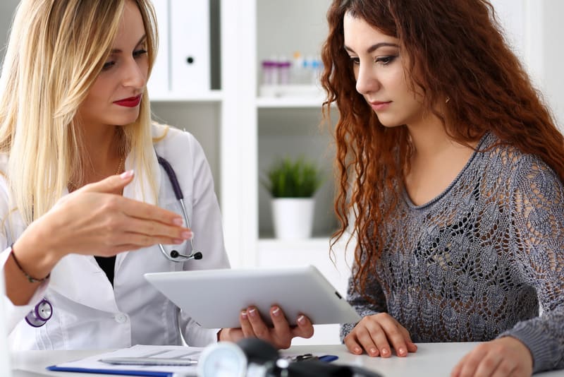 Beautiful female medicine doctor explain diagnosis to patient holding and showing digital tablet pc. Physical, disease prevention, 911, prescribe remedy, healthy lifestyle, modern technology concept