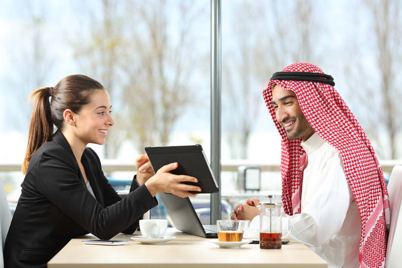 Businesswoman or saleswoman working with an arab man showing products in a tablet in a coffee shop
