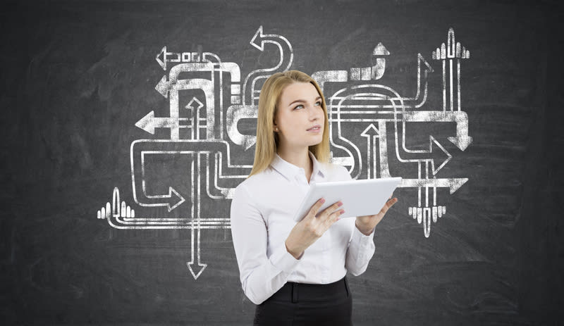 Blond girl with a tablet is standing near blackboard with tangled arrow sketch on it. Concept of looking for the answer