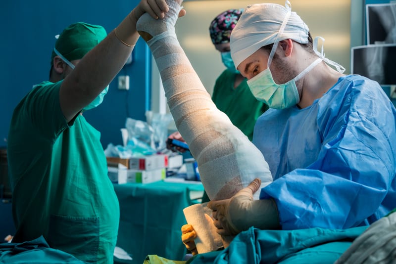 Orthopedic surgeon dressing patients leg in the operating room with compressing bandage after a total knee arthroplasty.