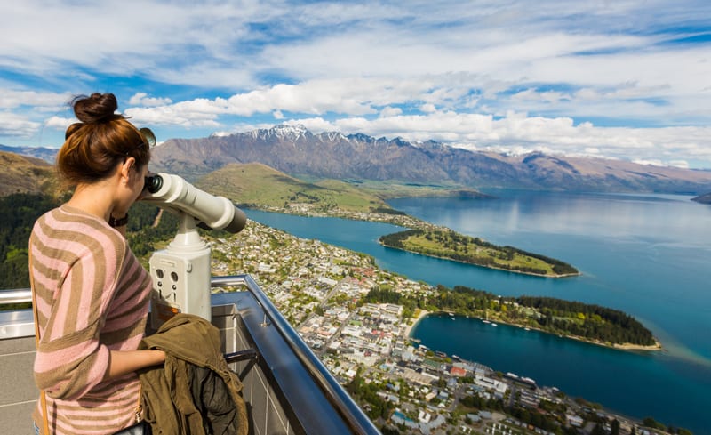 Young adult woman enjoy a stunning view of Queenstown through the binocular from view point of the Skyline Gondola