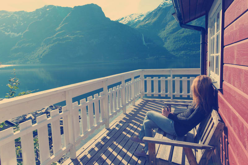 girl sitting near rorbu and admires the beautiful Norwegian landscape at the fjord and mountains