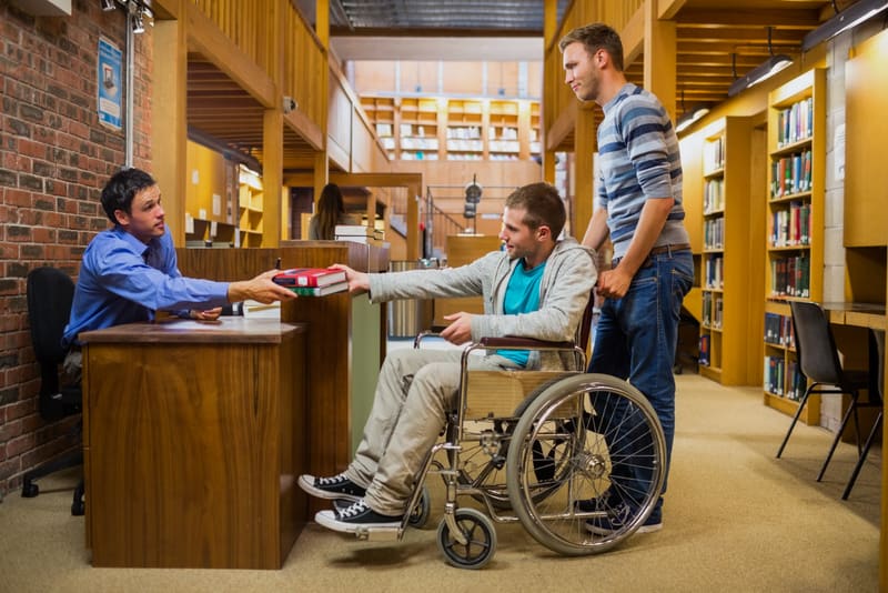 Side view of a male student in wheelchair at the counter in college library