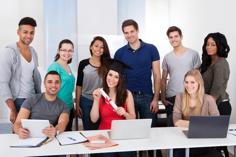 Portrait of university student holding degree with classmates standing in classroom