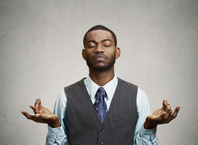 Young businessman meditating, eyes closed, isolated grey wall background. Stress relief techniques at work concept. Take a deep breath.