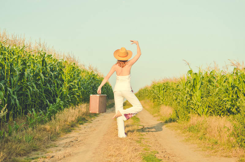Woman wearing hat standing in ballet pose on country road