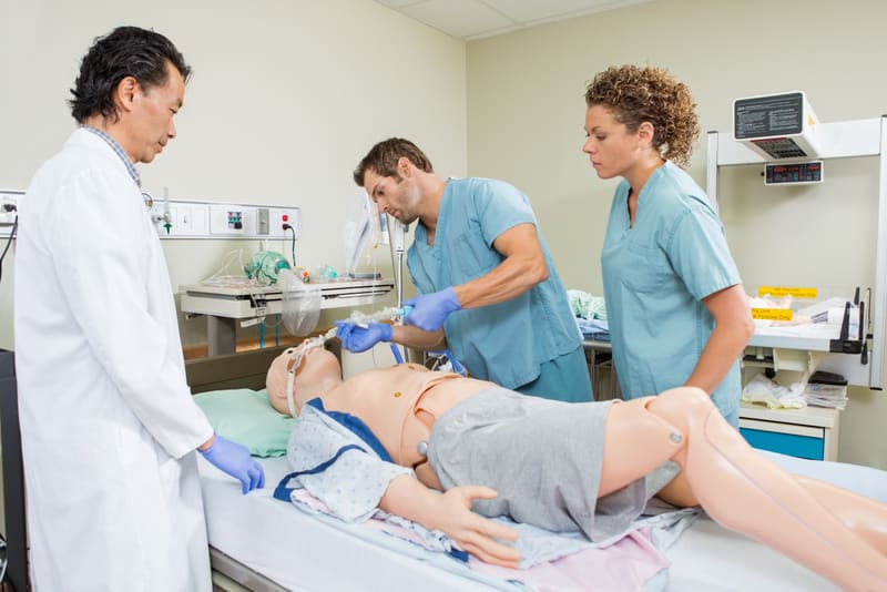 Male nurse adjusting endotracheal tube on dummy patient while colleague and doctor looking at it in hospital
