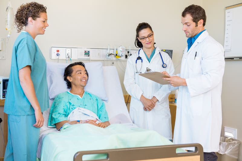 Young doctors discussing notes while nurse and patient looking at them in hospital room