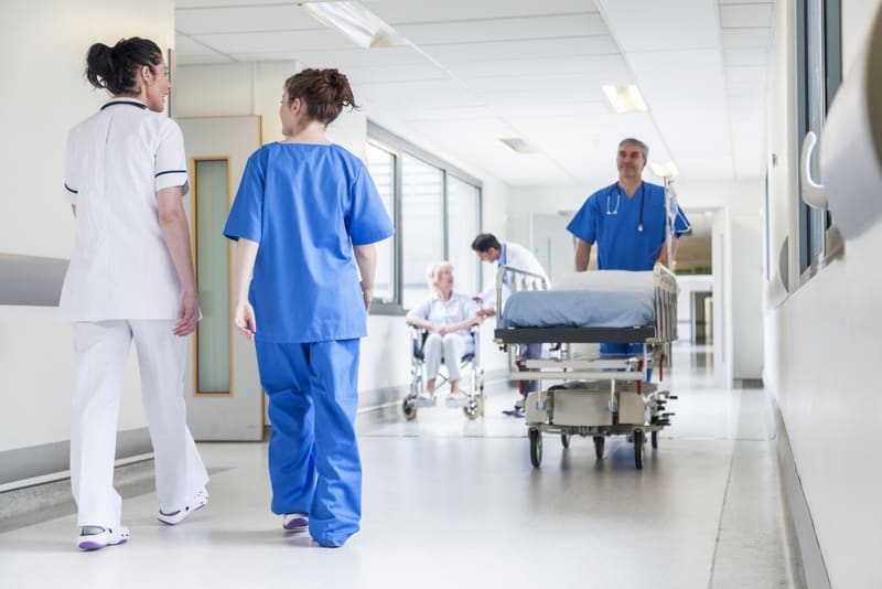 Male nurse pushing stretcher gurney bed in hospital corridor wit