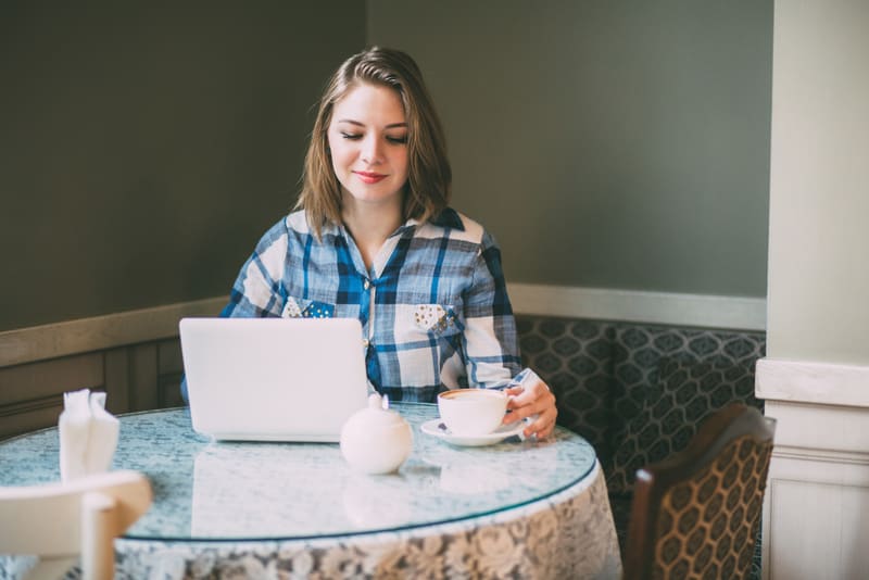 Young attractive businesswoman in plaid shirt wiorking with laptop in cafe.