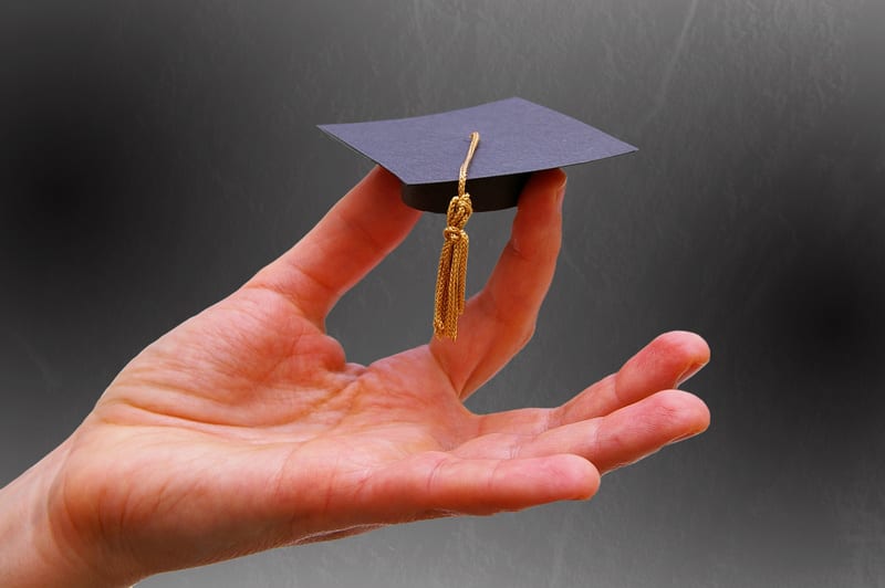 Person's hand holding a miniature graduation cap -- Education or career concept