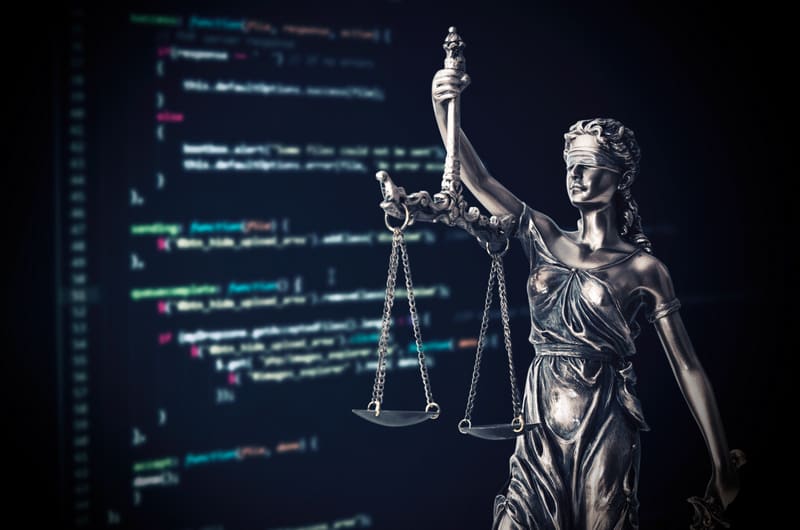 Justice statue with code on monitor device in background
