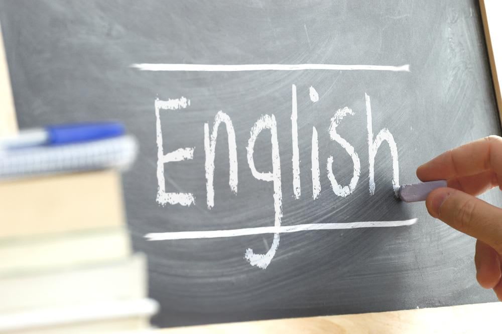 Hand writing on a blackboard in an language class with the word "English" wrote in. Some books and school materials.