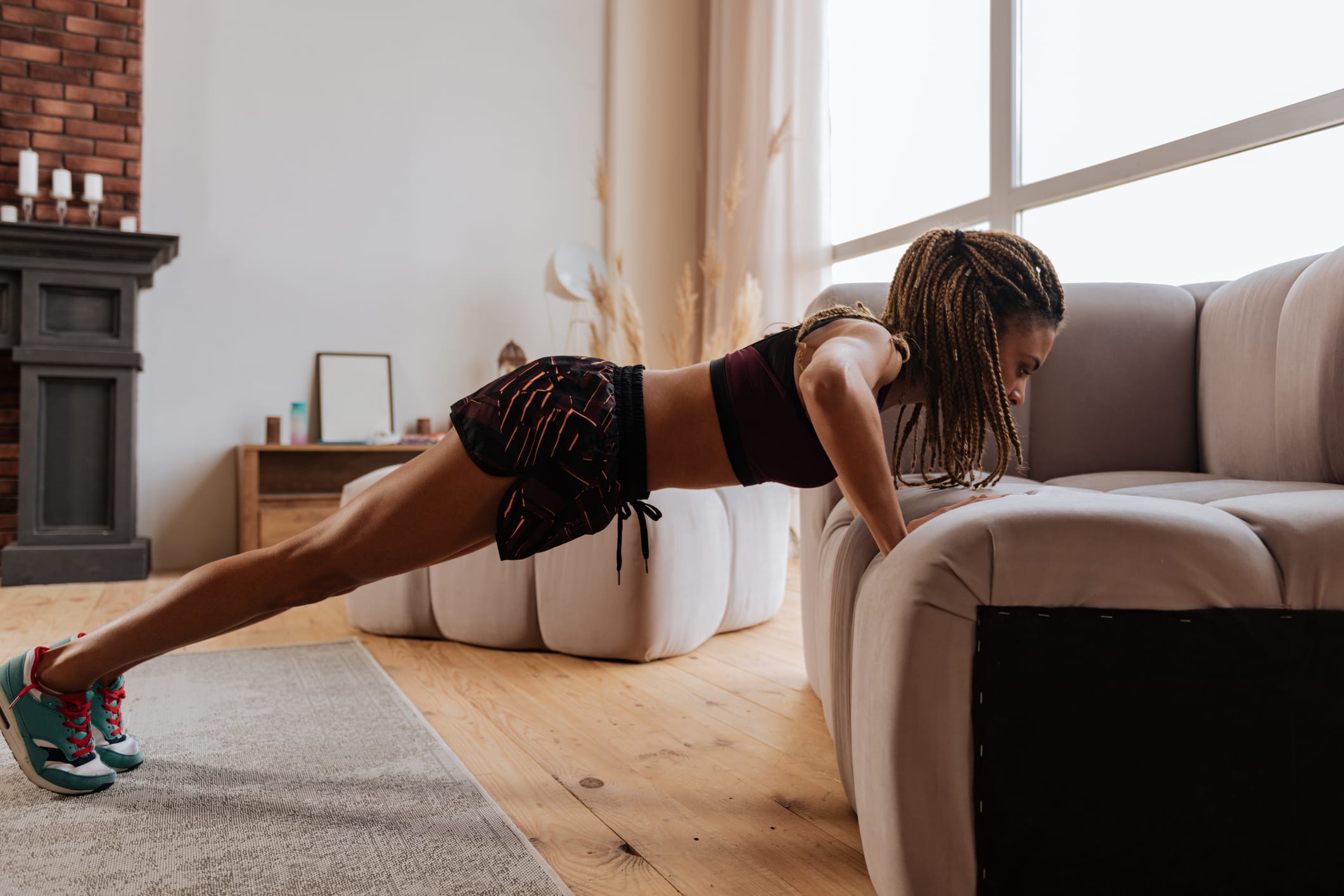 Woman wearing shorts and top doing pushups near sofa