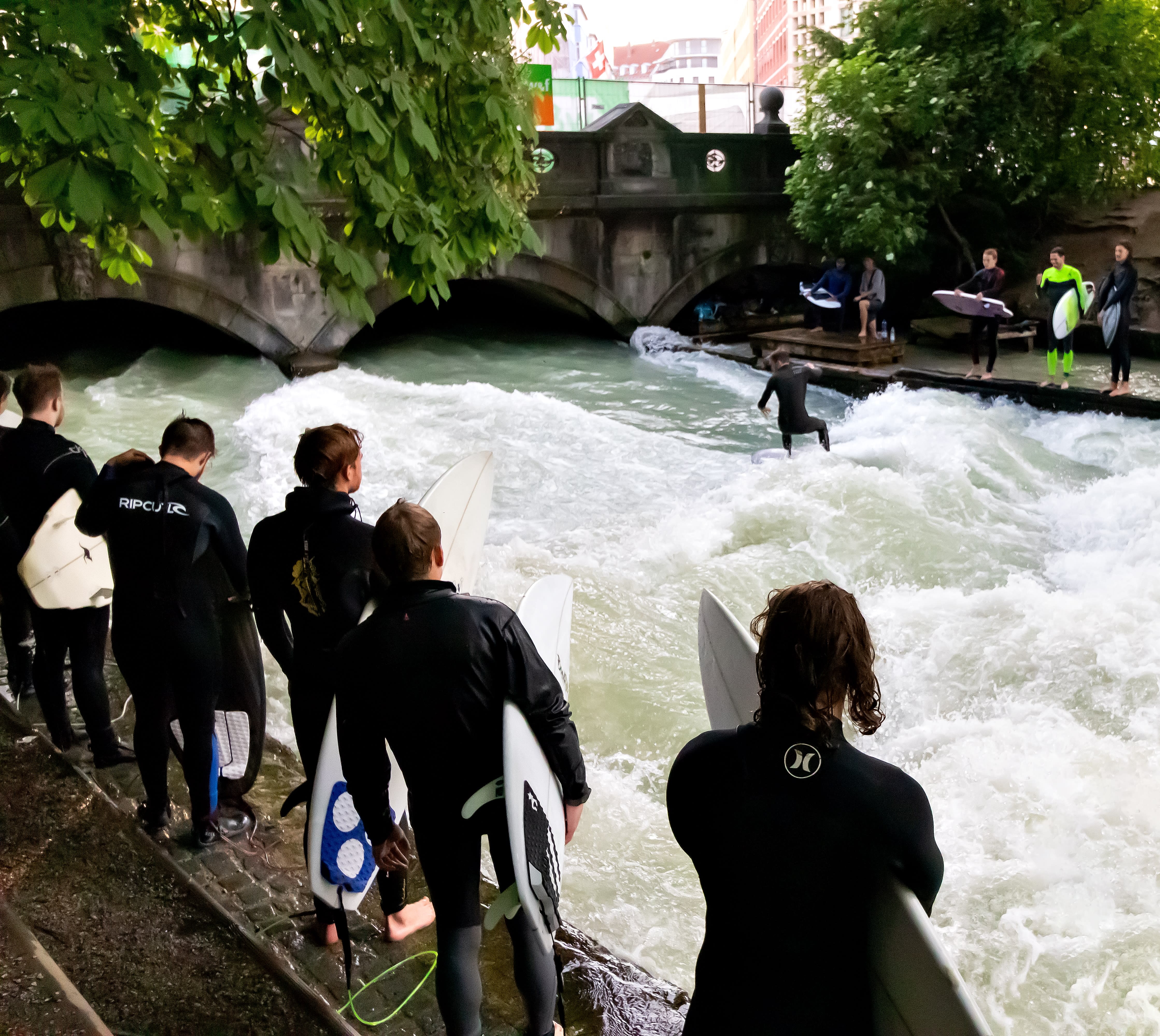 Surfers in Munich? Yes! Surfing waves on the Eisbach river at the entrance of the Englischer Garten.