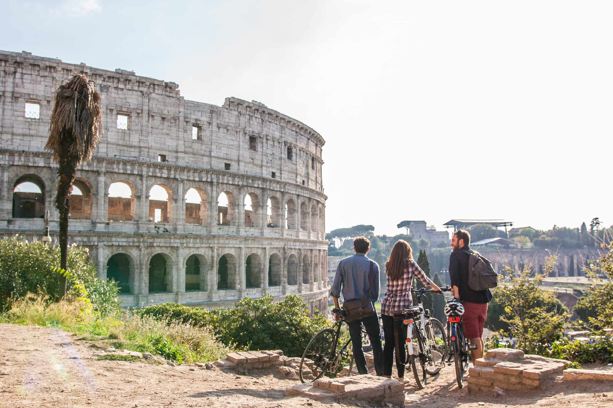 Three happy young friends tourists with bikes at Colosseum in Rome having fun
