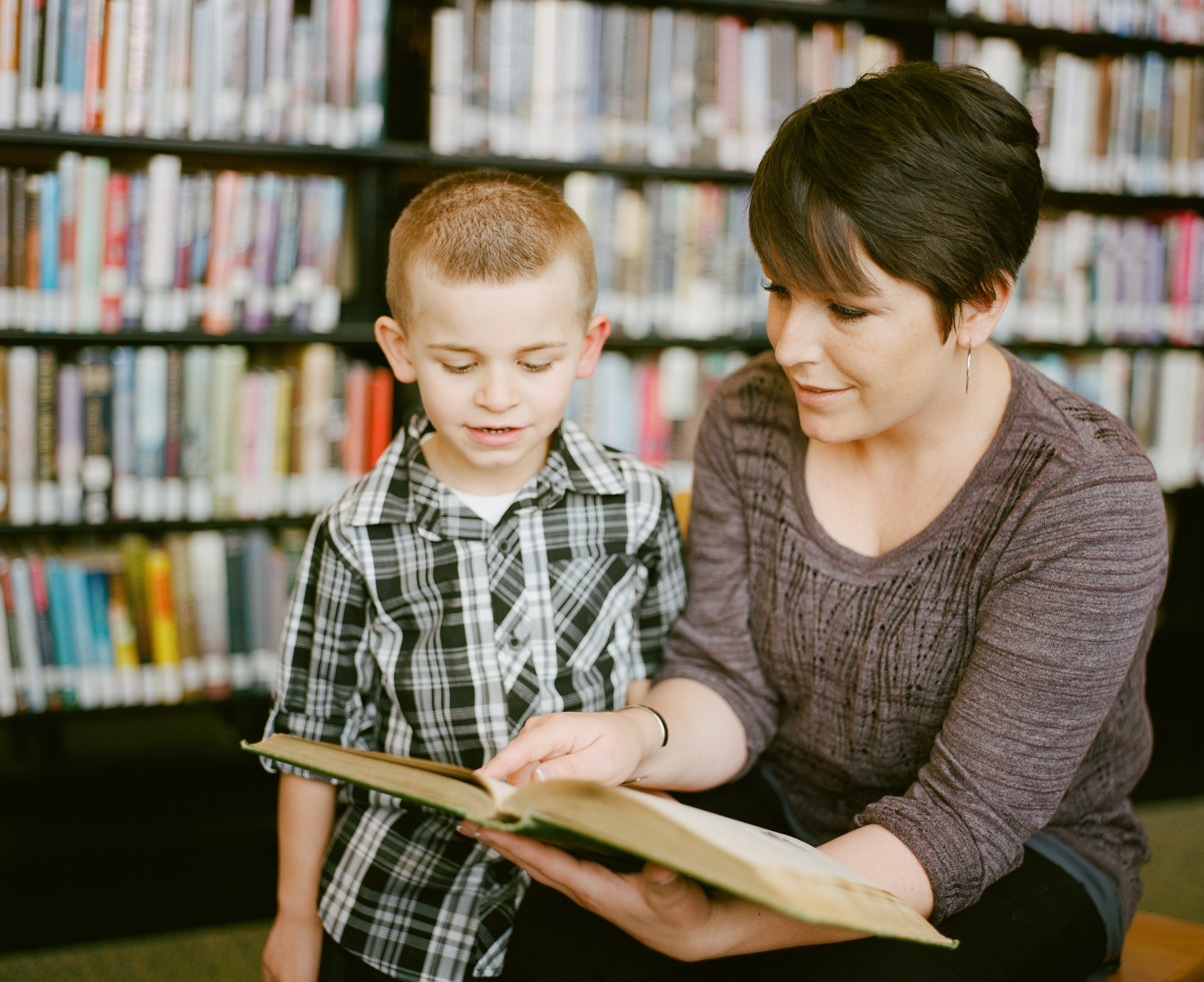 Mother reading to her son as he listens intently. Books in the background are slightly blurred creating the perfect atmosphere to instill a lifelong love of reading. The 3 - 6 year old boy is engaged, happy, the moment is captured in this photo creating a lifelong memory. https://www.awcreativeut.com https://www.instagram.com/AwCreativeUT/ #AwCreativeUT #awcreative #AdamWinger