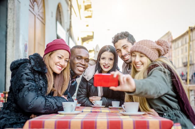 Five multi-racial friends taking a selfie with cellphone in a restaurant bar - Young students having fun and sitting at a table, drinking hot drinks