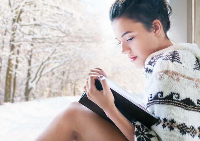 Beautiful young brunette woman reading book wearing knitted ponc