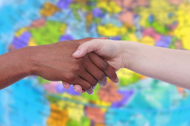 Afrikanerin und Europerin geben sich die Hand vor Weltkarte