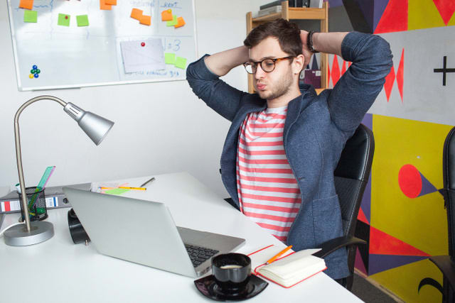 Young hipster male in modern office with hands over his head with laptop