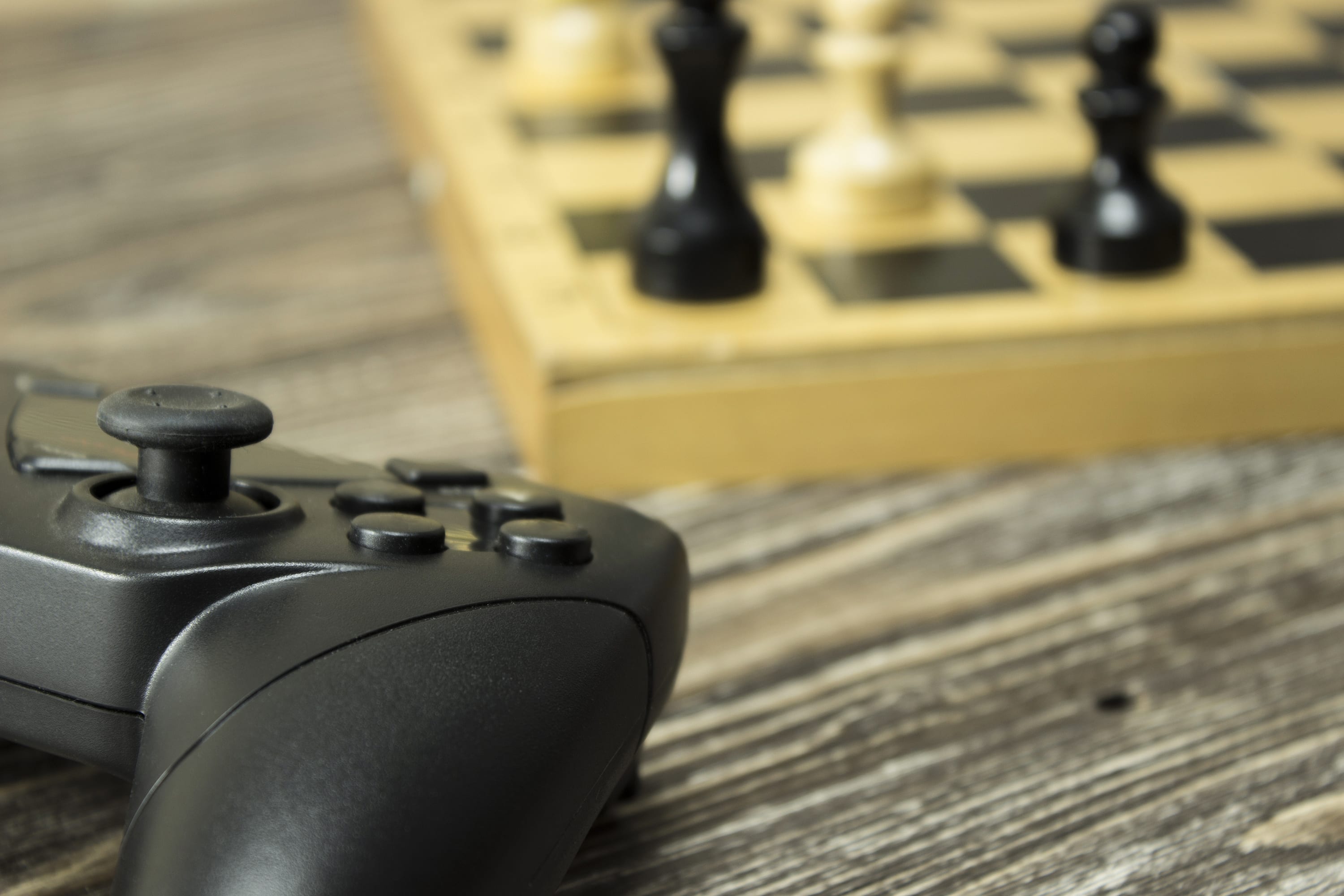 Gamepad and chess board with figures on the wooden background. Focus on gamepad