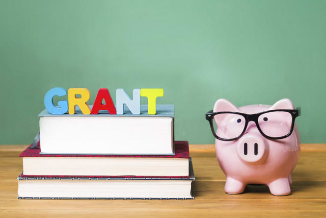 Education grant theme with pink piggy bank on top of books with chalkboard in the background