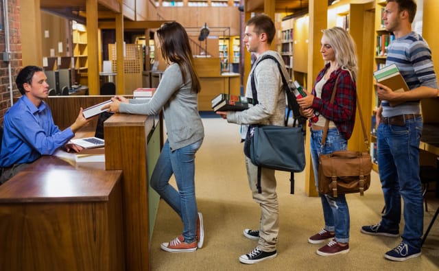 Side view of young students in a row at the counter in college library