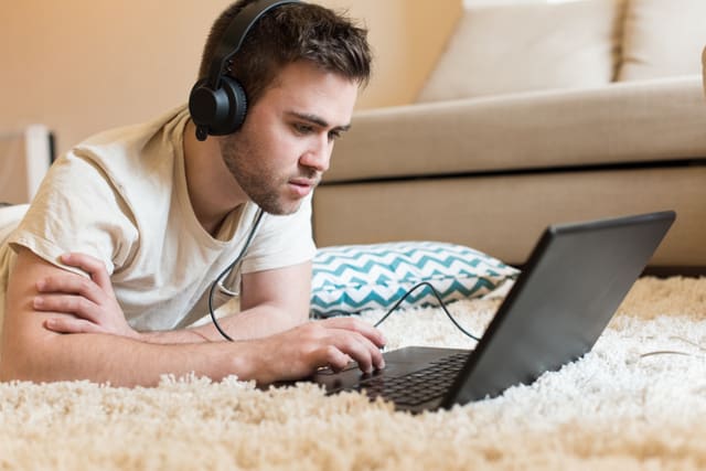 Man lying on the floor using headphones on laptop