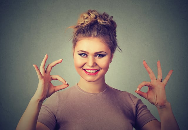 Excited happy young optimistic woman giving ok sign gesture with two hands isolated on gray wall background. Positive human emotions face expression body language