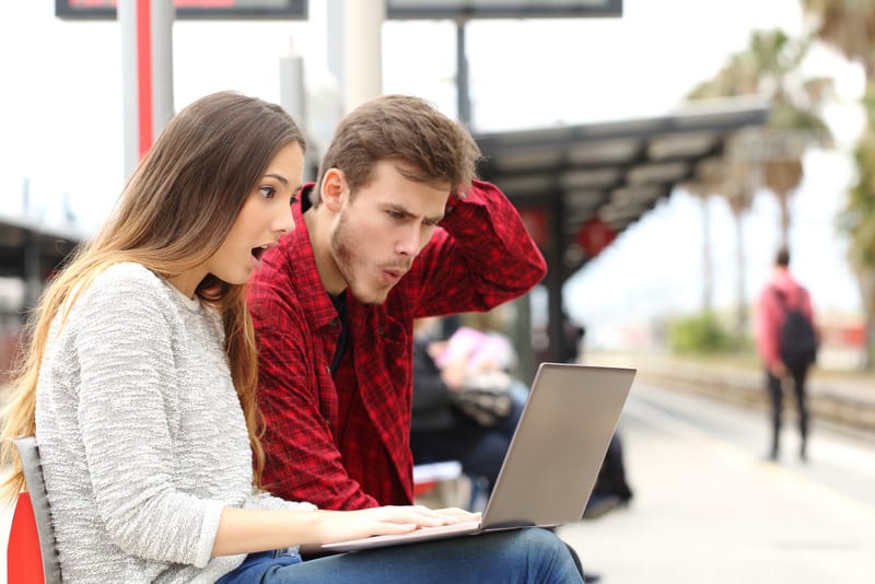 Couple worried and surprised watching a laptop in a train station while they are waiting
