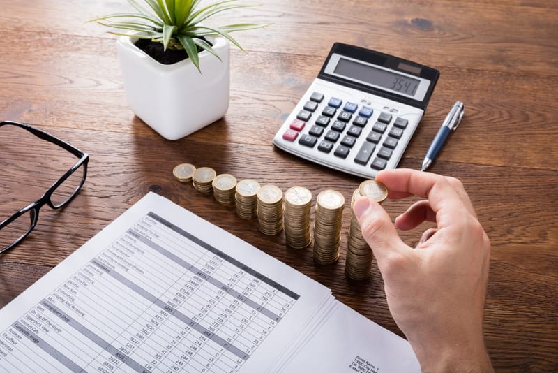 Person Stacking Coins With Calculator On Wooden Desk. Investment And Insurance Concept