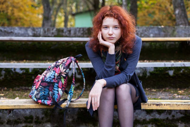 Portrait of a ginger woman sitting on the bench in the city park in a ensive pose