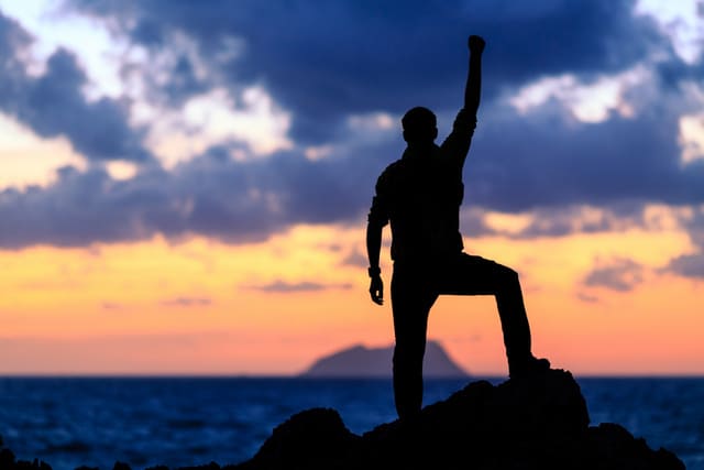 Success achievement running or hiking accomplishment business and motivation concept with man sunset silhouette celebrating with arms up raised outstretched trekking climbing trail running outdoors in nature