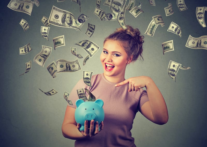 happy woman with piggy bank ecstatic celebrates success under a money rain falling down dollar bills banknotes