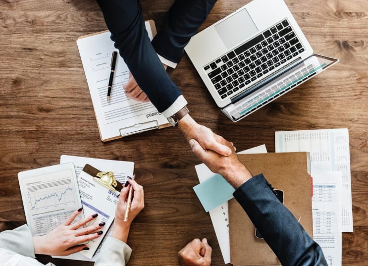 two people handshaking above table with laptop two people handshaking above table with laptop