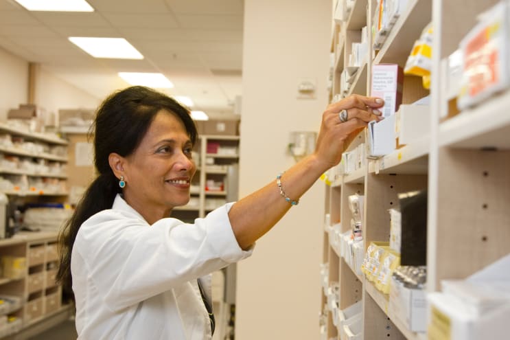 A female pharmacist is selecting a drug from the pharmacy inventory. A female pharmacist is selecting a drug from the pharmacy inventory.
