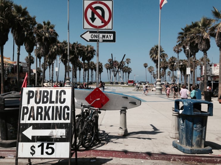Public Parking sign with price in front of a pedestrian area near the beach.